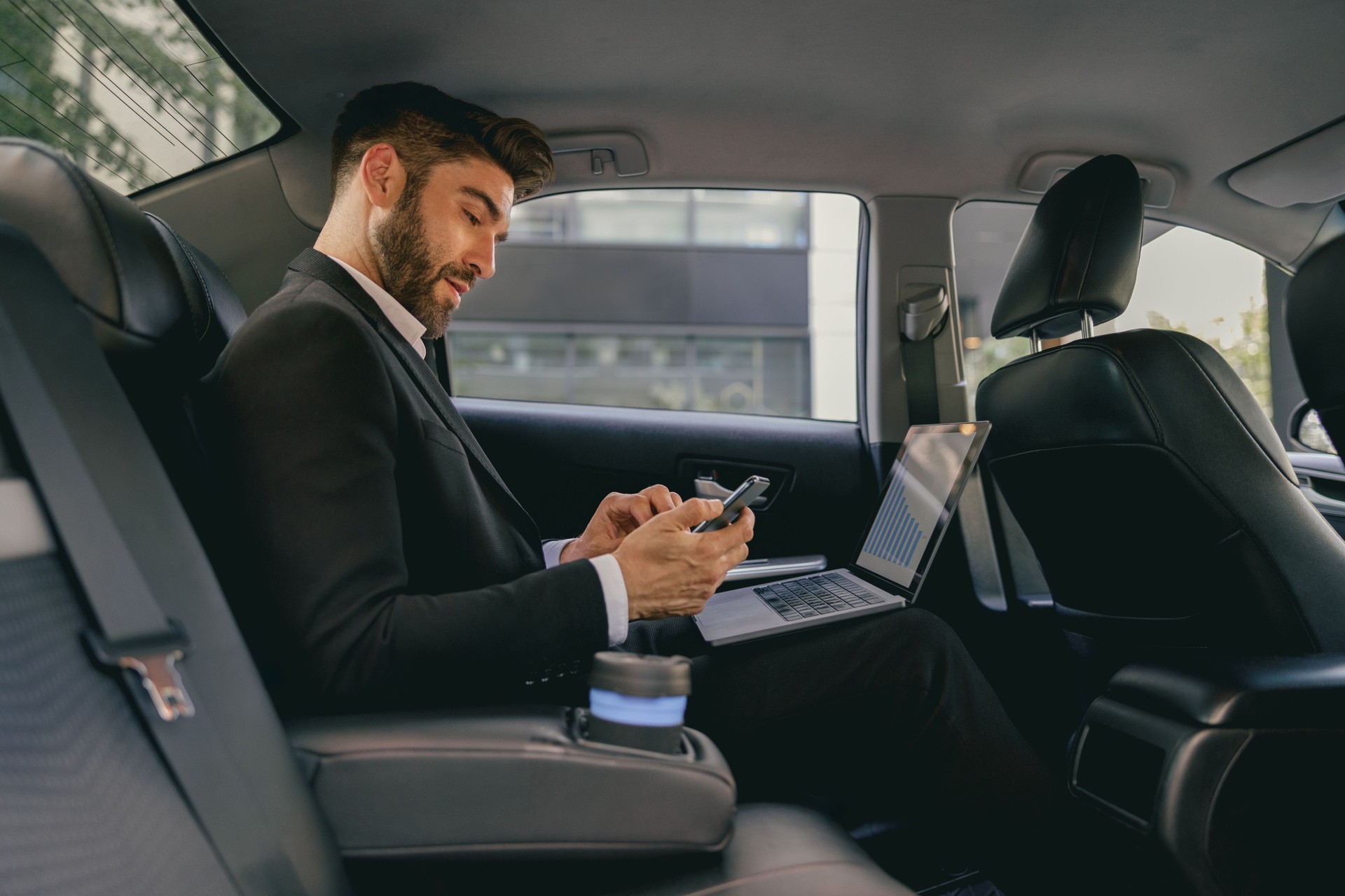 Busy male analyst working on laptop and use mobile phone while going to airport by car